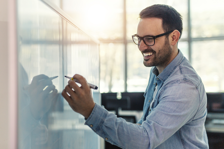 Smiling man drawing on whiteboard explaining configuraiton management CM definition